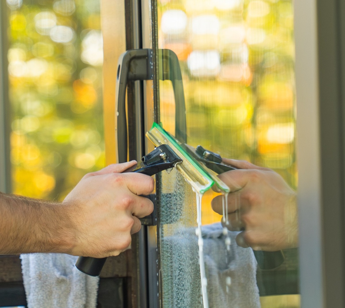 Close-up of a squeegee pulling soapy water off a glass door