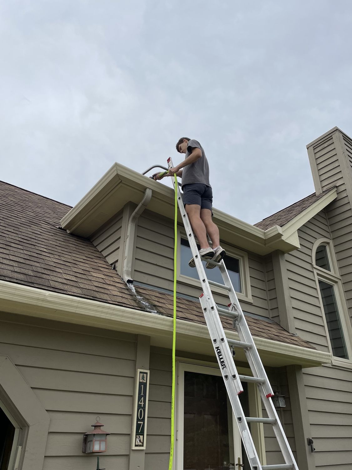 Technician clearing a gutter by hand from a ladder
