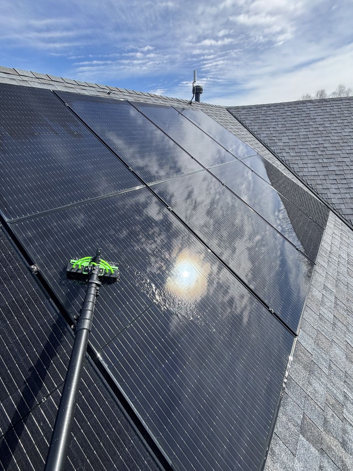 Rooftop solar panels being cleaned with a soft-bristle brush on an extension pole